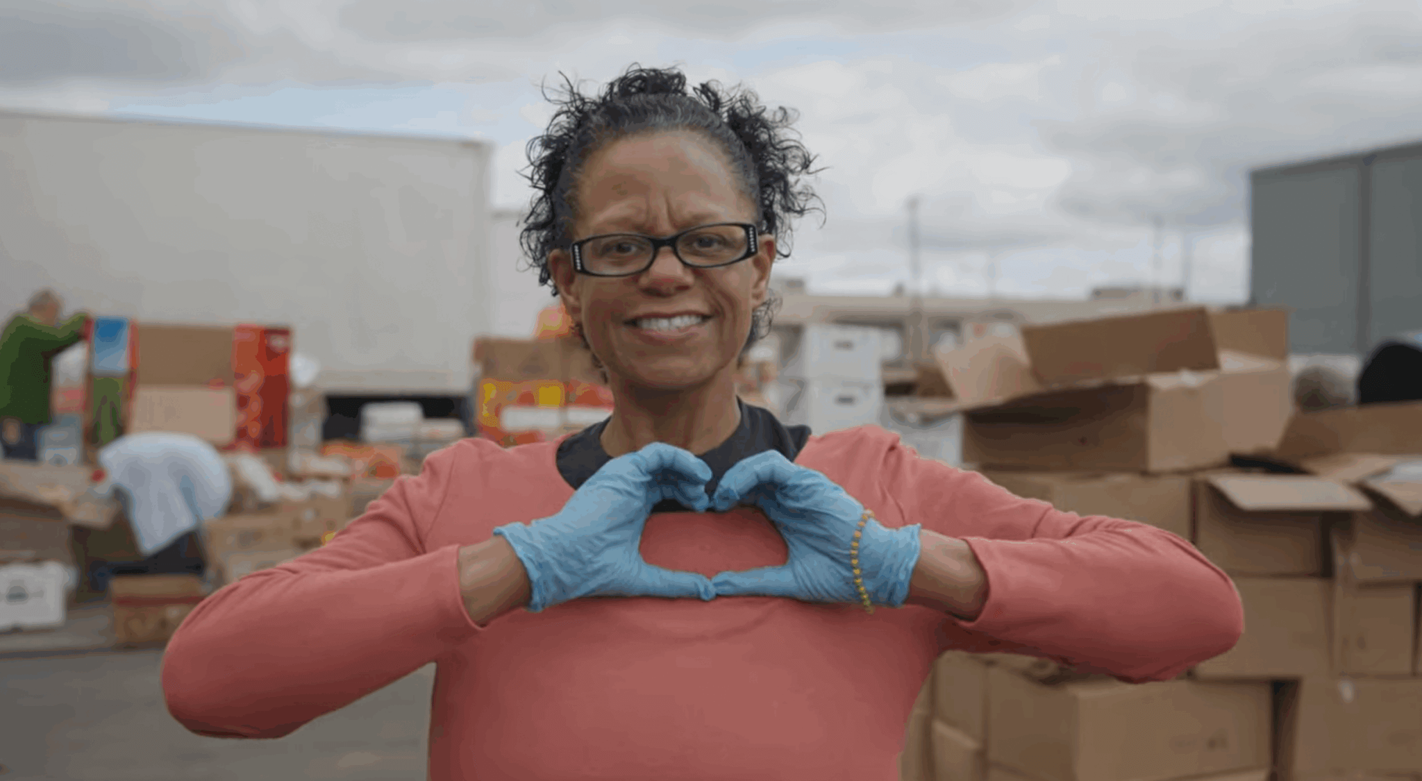 Volunteer placing hands in heart formation while volunteering at our Friday Community Distribution Program.